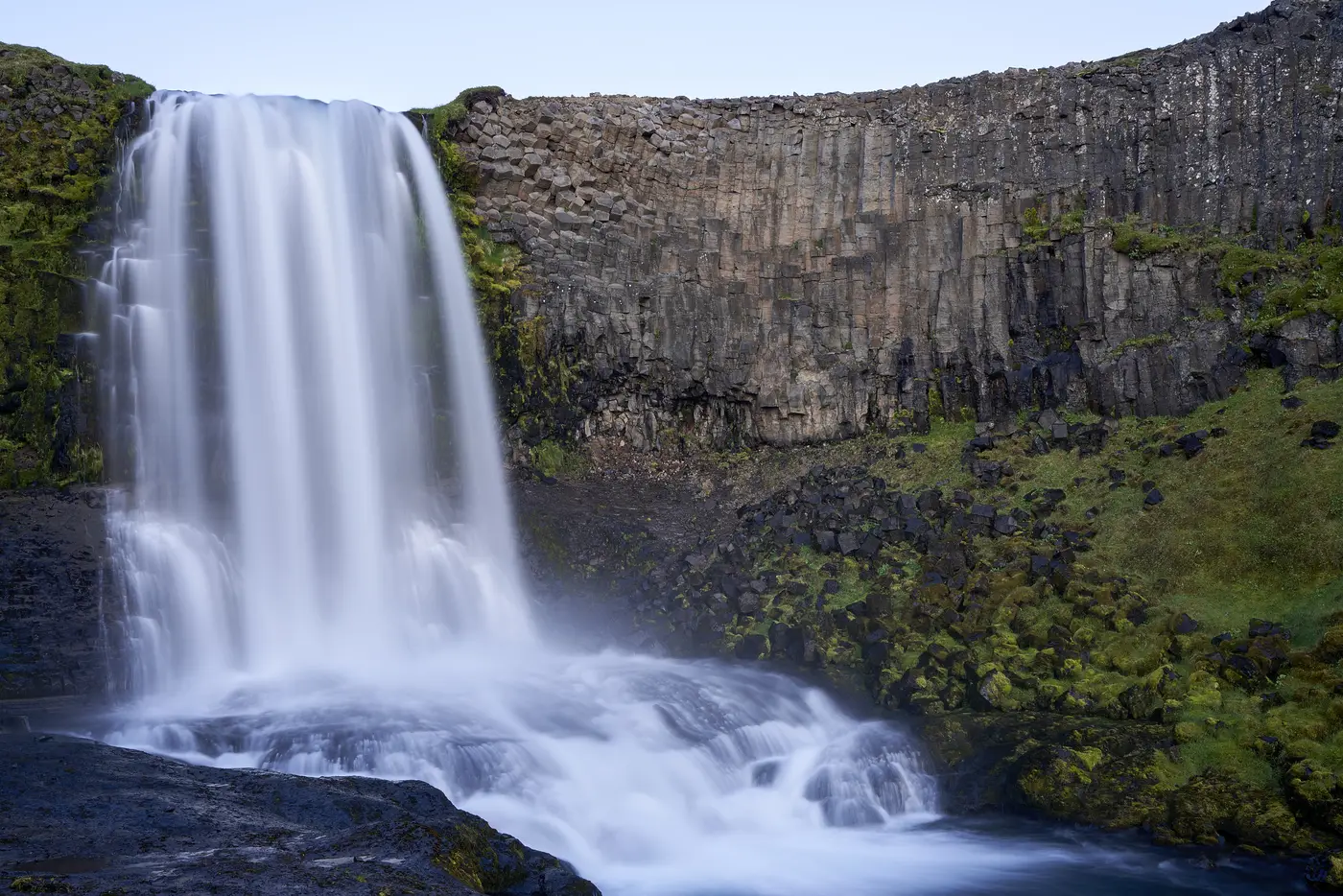 A tall waterfall against a green cliff