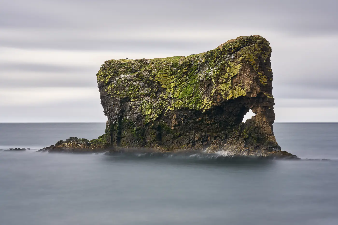 A moss-covered rock arch in the sea