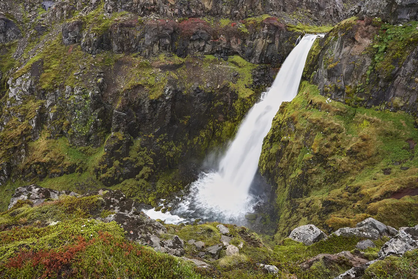 A slender tall waterfall against a green cliff