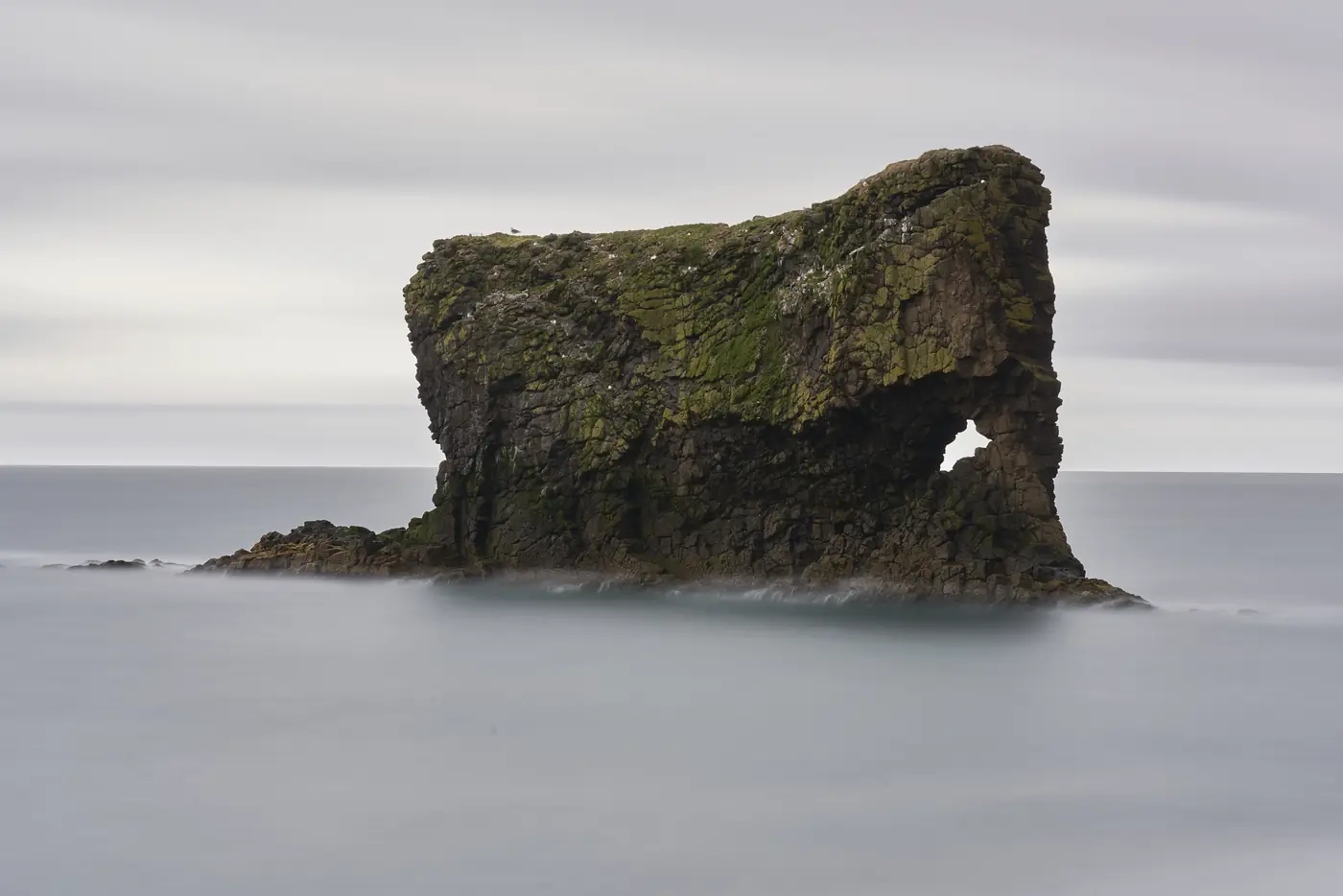 A dark rock arch on the coast